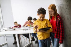 Best friends standing in front of kids programming electric toys and robots at robotics classroom photo