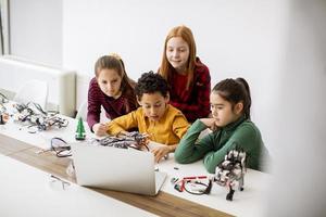 Niños felices programando juguetes eléctricos y robots en el aula de robótica foto