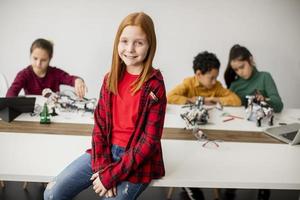 Cute little girl standing in front of kids programming electric toys and robots at robotics classroom photo