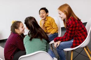 Portrait of cute little kids in jeans  talking and sitting in chairs against white wall photo