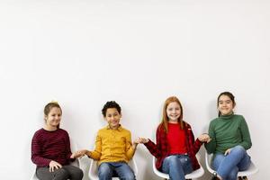 Retrato de lindos niños en jeans sentados en sillas contra la pared blanca foto