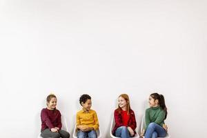 Portrait of cute little kids in jeans  sitting in chairs against white wall photo