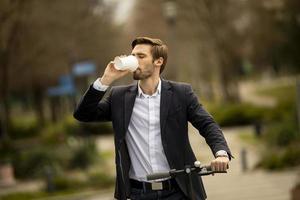 Joven empresario con taza de café para llevar en scooter eléctrico foto