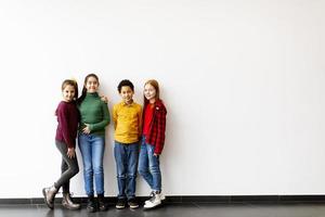 Portrait of cute little kids in jeans looking at camera and smiling standing against white wall photo