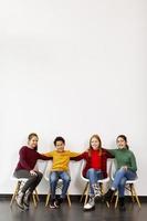 Retrato de lindos niños en jeans sentados en sillas contra la pared blanca foto