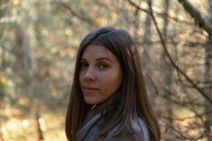 Half turned girl in a gray coat which stands in the forest on a sunny autumn day photo