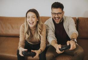 Pareja joven jugando videojuegos en casa sentado en el sofá y divirtiéndose foto