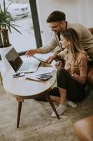 Young woman and young man using laptop while sitting by sofa at home photo