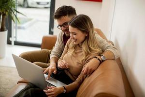 Young couple using laptop together while sitting on sofa at home photo