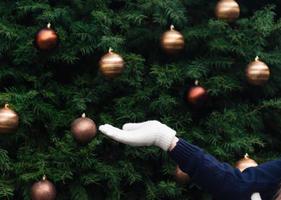 Girl's hand in a white mitten empty on the background of a Christmas tree photo