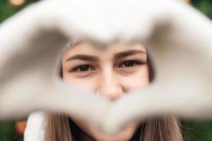 Close-up portrait of woman wearing a santa claus hat with emotion and making heart photo