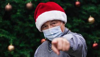 Close-up portrait of senior man wearing a santa claus hat and medical mask with emotion