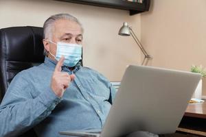 Senior man in face mask working or communicating on laptop at home photo