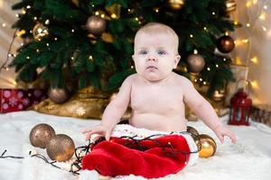 Adorable baby without clothing on santa claus hat on a background of Christmas balls photo