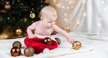 Adorable bebé con ropa sin sombrero de santa claus sobre un fondo de bolas de navidad foto