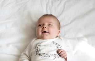 A close-up portrait of a baby girl who lies in bed and smiles