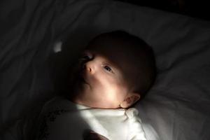 A close-up portrait of a baby girl lying on a bed in the sun photo