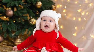 A cute little girl in a red dress and white hat expresses emotions photo