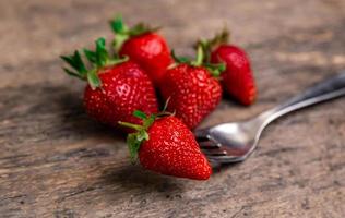 Fresh strawberries and one berry on fork still life on dark wooden background photo
