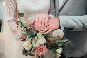 Manos con anillos de la novia y el novio están acostados en el primer ramo de flores