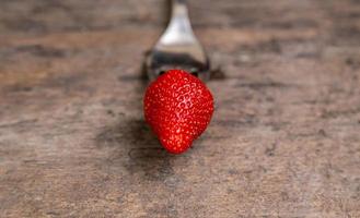 One strawberry on golden fork on wooden non paint background photo
