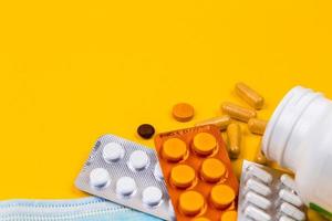 Máscara médica protectora sobre fondo amarillo rodeado de pastillas de colores foto