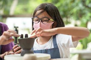 Closeup dirty face of an Asian girl with eyeglasses learning how to mold the clay work in a workshop classroom. photo