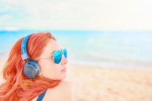 Beautiful woman in sunglasses listening to music on the beach photo