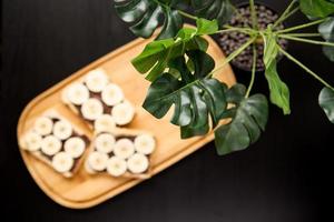 Three banana white bread toasts spread with chocolate butter on a chopping board with leaves on a dark background photo