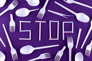 The word stop made of plastic tubes on a purple background with plastic utensils photo