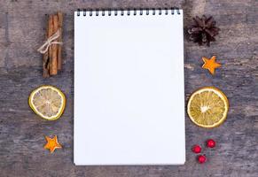 A pile of cinnamon sticks dried orange and tangerine stars on old wooden table with white empty piece of paper photo