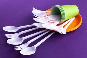 Bright orange and green set of disposable plastic tableware on purple background photo