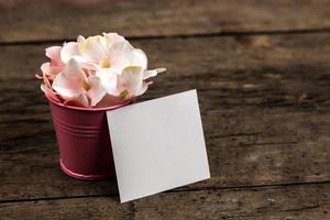 Pastel pink hydrangea flowers in a little bucket and a piece of paper on wood background photo