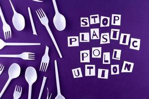 The word stop plastic pollution made of cut paper on a purple background with plastic utensils environmental pollution concept photo