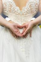 cuatro manos forman un corazón en la parte posterior de un vestido de novia foto