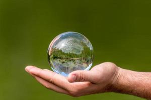 Bola de cristal con espejo de árboles y el cielo del lago se encuentra en una mano contra el fondo verde foto