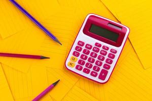 Calculator on orange sheets of paper with pencil photo