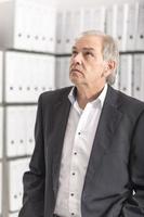 Middle aged man with white shirt is standing in front of a shelf wall with documents photo