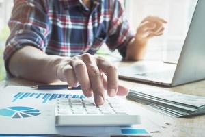 The accountant is pressing the calculator to calculating check the accuracy of the investment budget with using computer laptop and document data to analysis photo