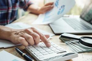 The accountant is pressing the calculator to calculating check the accuracy of the investment budget with using computer laptop and document data to analysis photo