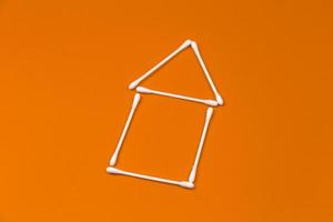 Cotton ear sticks arranged as a little house on orange background photo