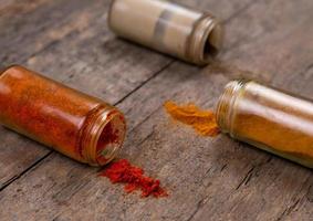 Chilli colorful powder spices scattered from bottle on wooden background photo