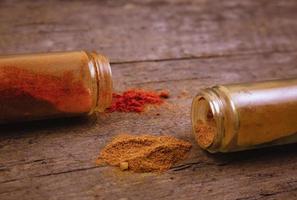 Chilli colorful powder spices scattered from bottle on wooden background photo