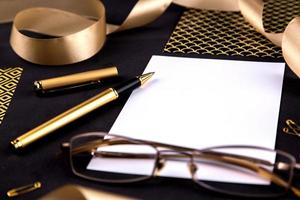 Gold pen ribbon paper clips and stationery on a black background with a white sheet of paper with copy space photo