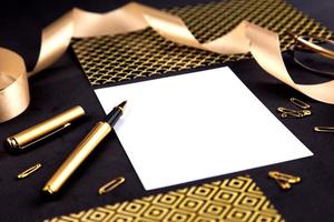 Gold pen, ribbon, paper clips and stationery on a black background with a white sheet of paper with copy space photo