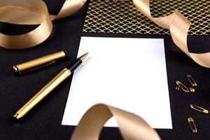 Gold pen, ribbon, paper clips and stationery on a black background with a white sheet of paper with copy space photo