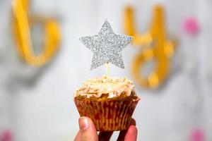 mano de niña sostiene cupcake de arándano con adorno de estrella de brillo plateado foto