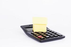 Concepto de préstamos hipotecarios con casa de papel amarillo y calculadora negra sobre fondo blanco. foto