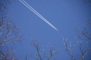 Airplane flying across a clear blue sky with trees photo