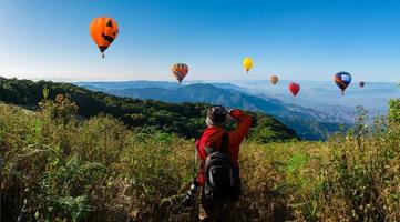 Fotógrafo profesional toma fotografías de paisajes en una montaña con globos aerostáticos en el fondo